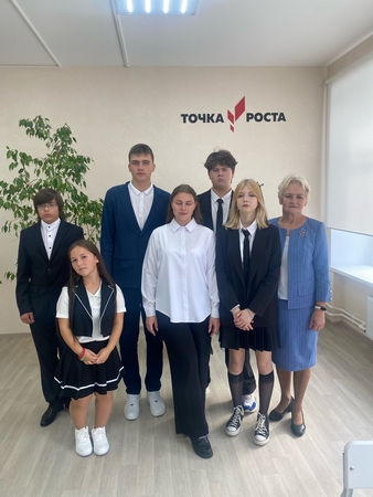 На изображении семь человек в помещении с надписью «Точка Роста» на стене. Пол светлый, есть зелёное растение..